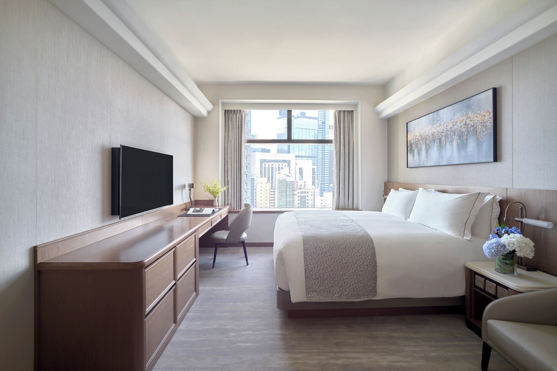 Une chambre d’hôtel avec un grand lit, un bureau doté d’un téléviseur à écran plat, une chaise et une vue sur la ville par la fenêtre.