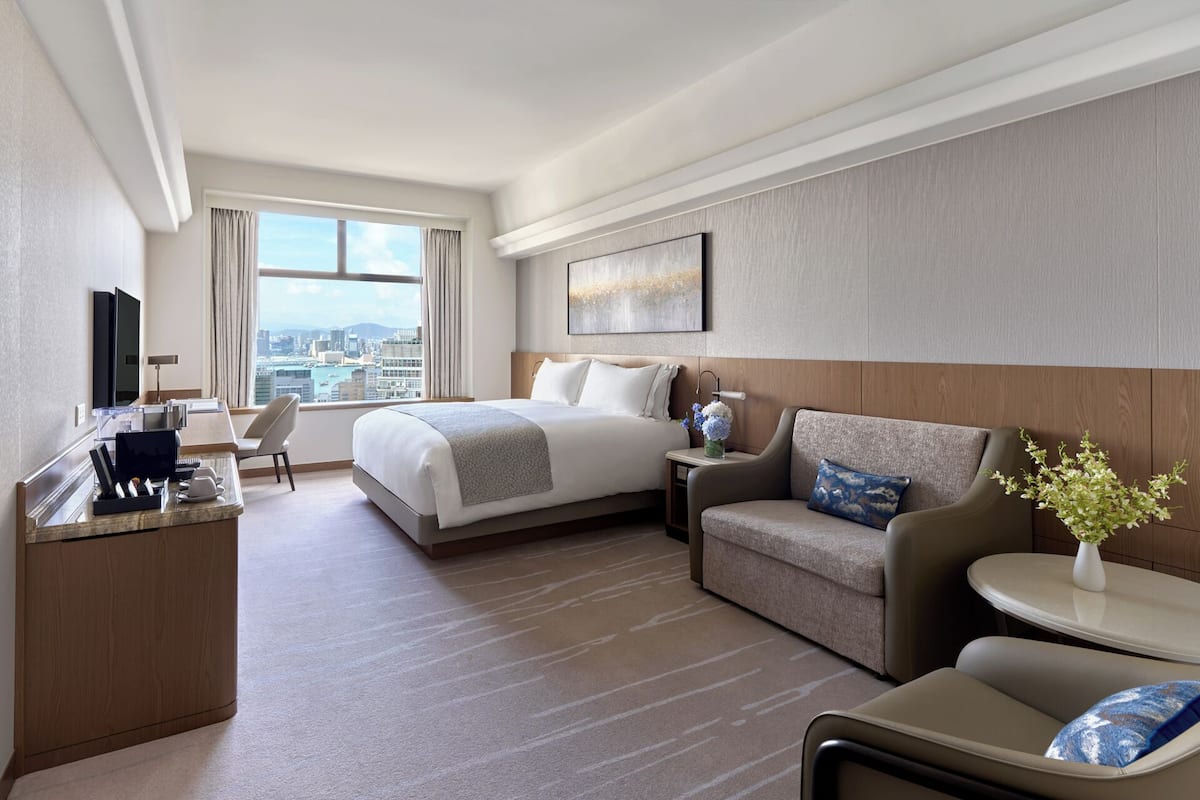 A hotel room with a bed, a desk, a sofa, and a view of the city.