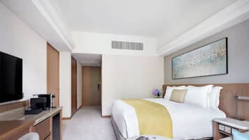A hotel room with a bed, a TV, a coffee machine, a desk, and a bedside table with a cup and a book.