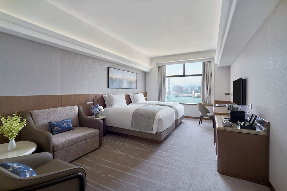 A hotel room with a large bed, a desk, a chair, a sofa, and a view of a cityscape.