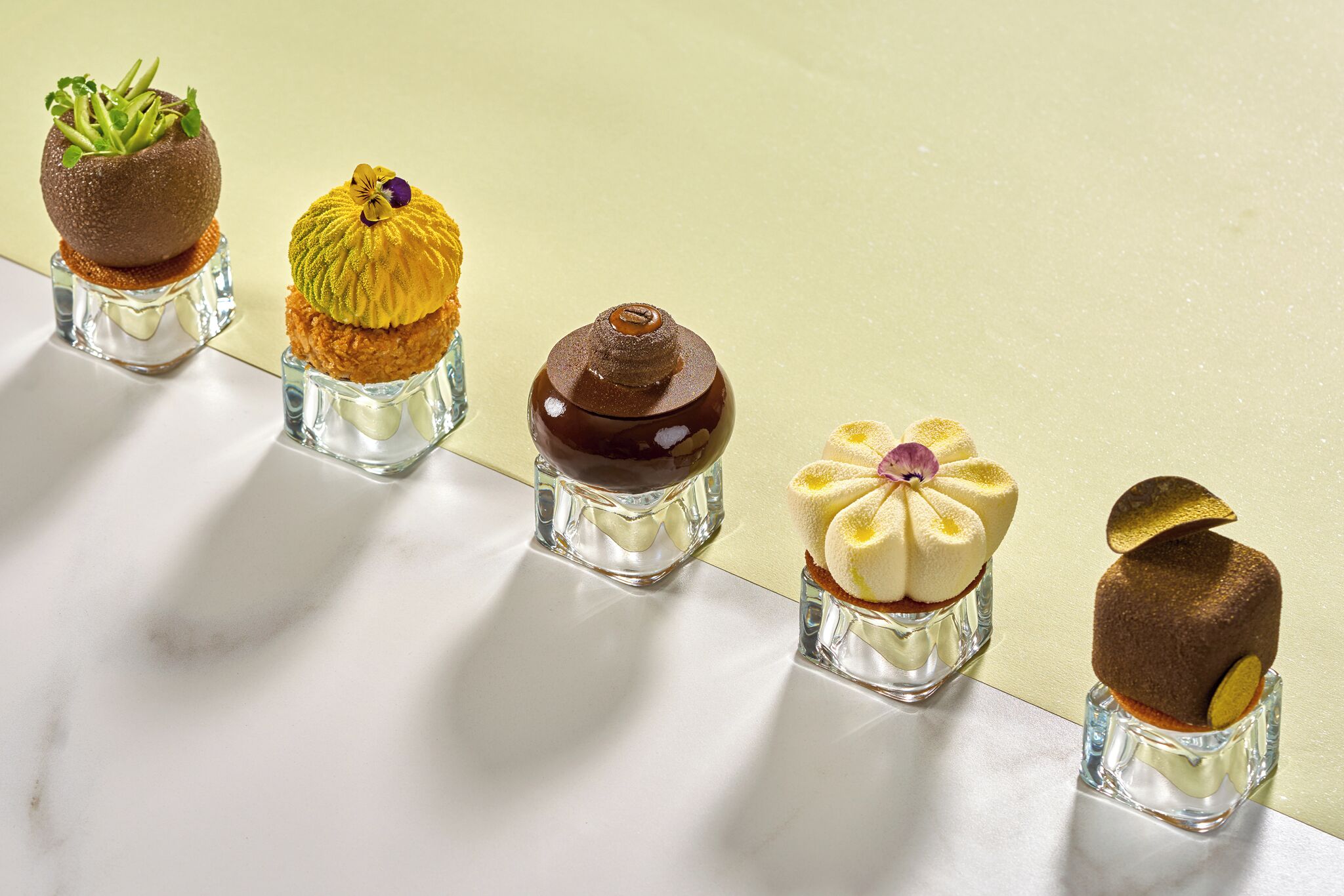 Cinq sortes de desserts présentées sur des présentoirs en verre transparent.