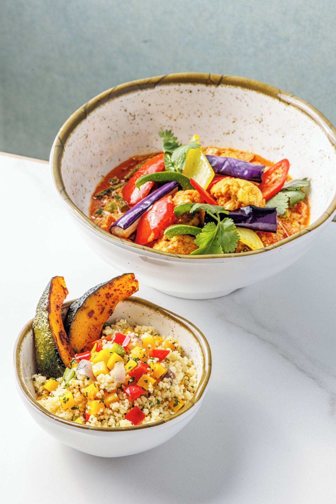 Deux bols de nourriture : l’un contient un plat de curry et des légumes, et l’autre, du couscous et des légumes.