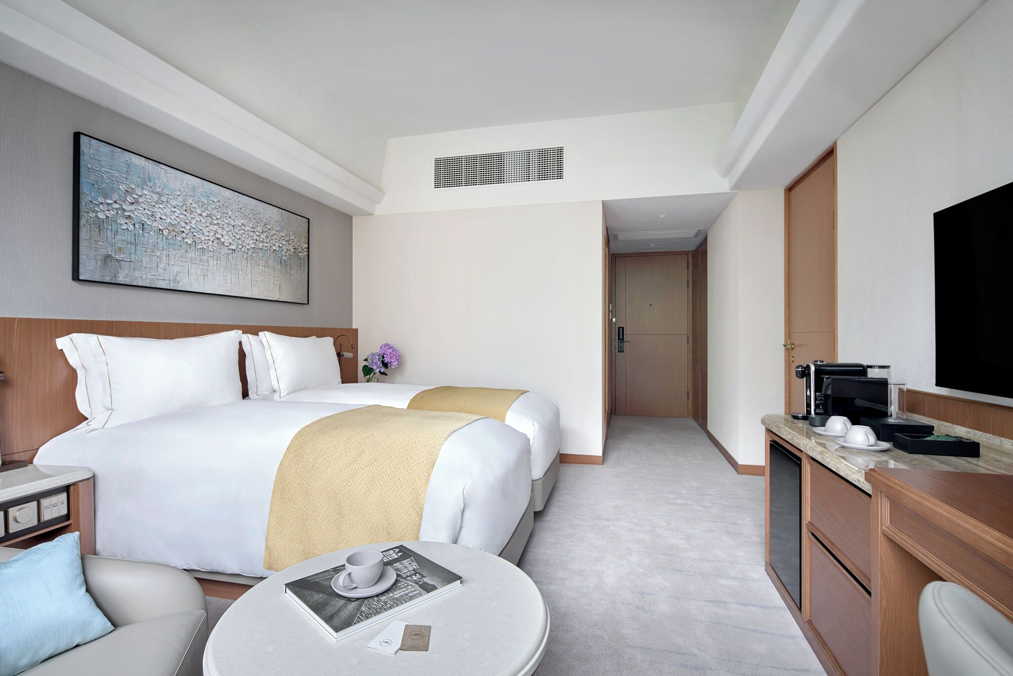 A hotel room with two beds, a dining table, a coffee maker, and a television.
