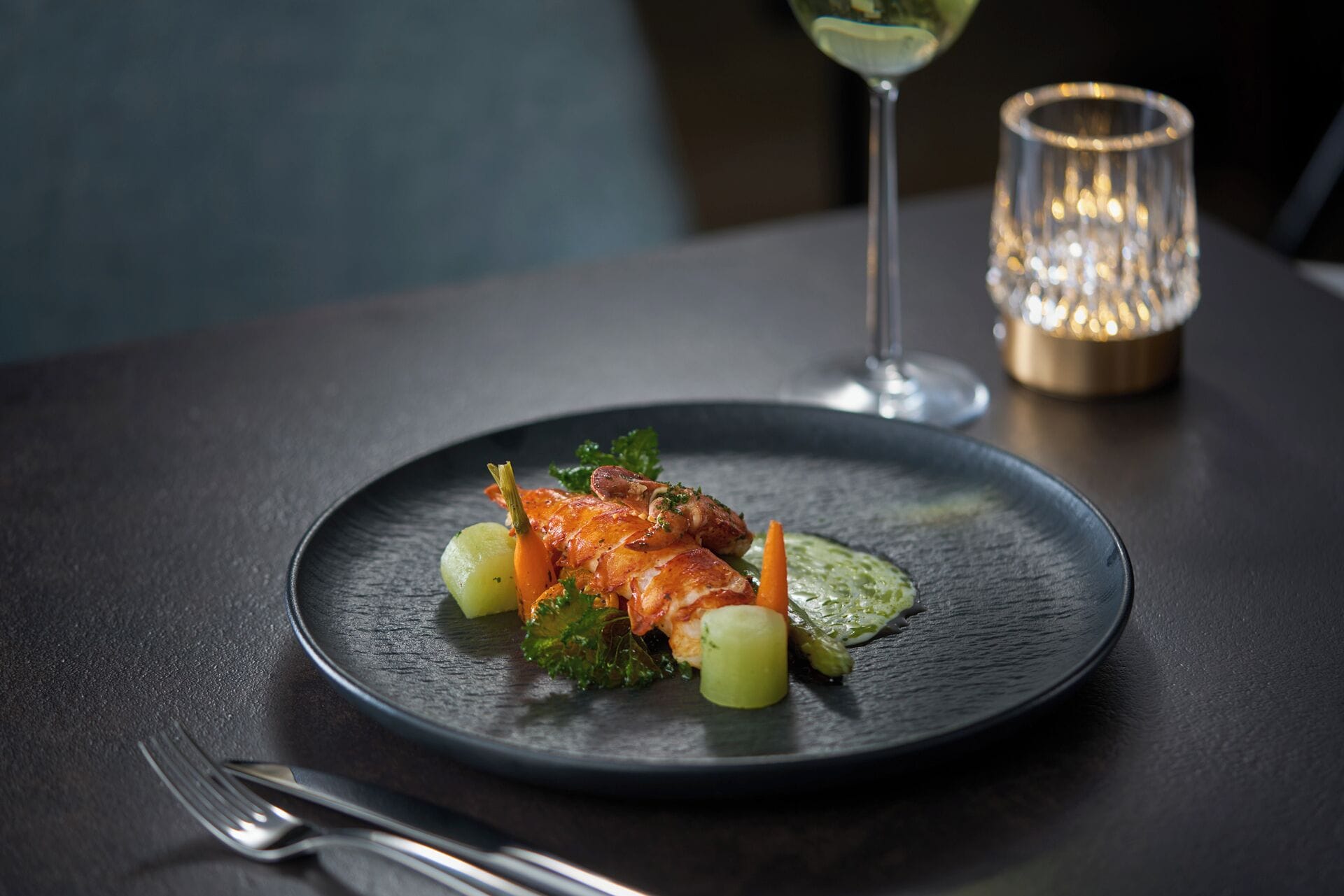 A plate of food on a dark table with a fork and a candle in the background.