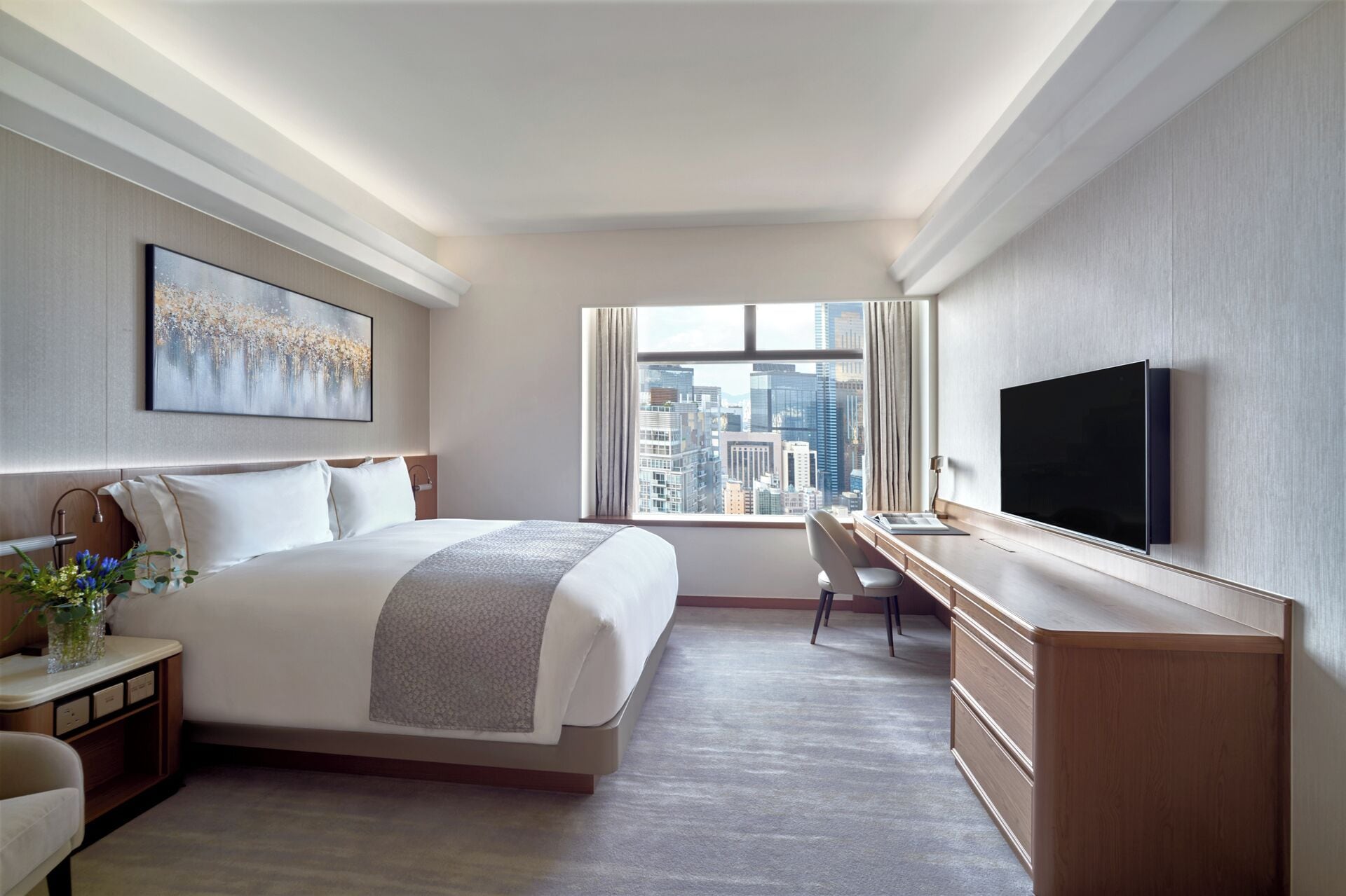 A modern hotel room with a large bed, a desk, a TV, and a city view.