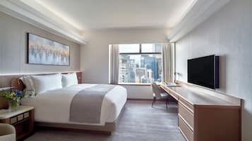 A modern hotel room with a large bed, a desk, a TV, and a city view.