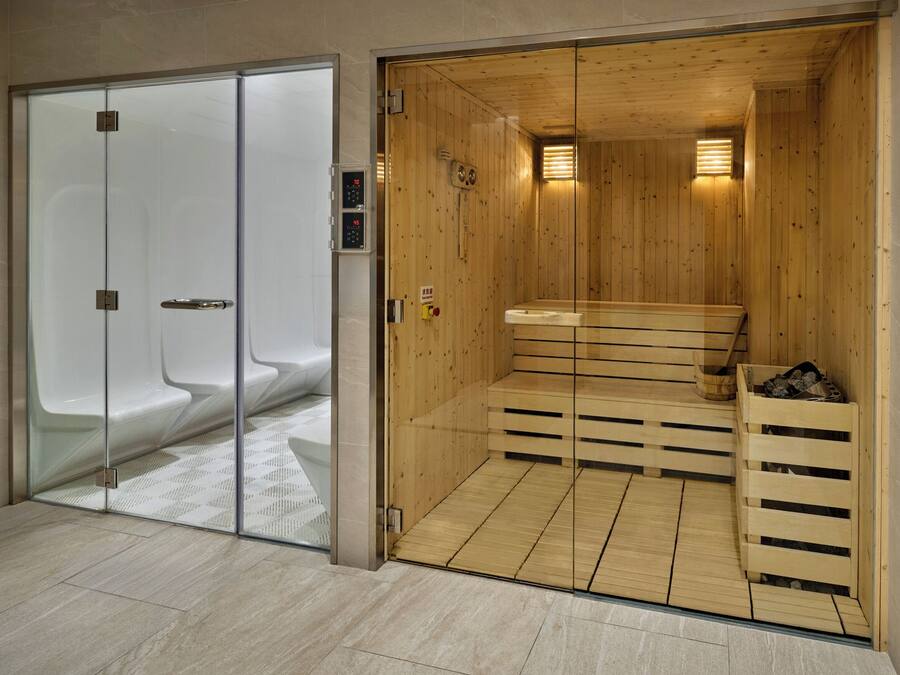 A sauna room with wooden benches and a glass door leading to a shower area.