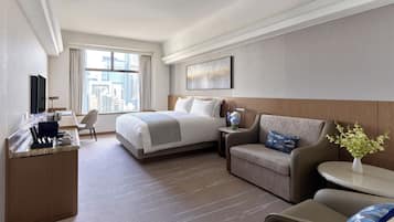 A hotel room with a bed, a desk with a computer, a sofa, and a small table with a vase.