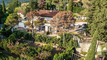 A villa with a red-tiled roof, surrounded by dense greenery and trees.