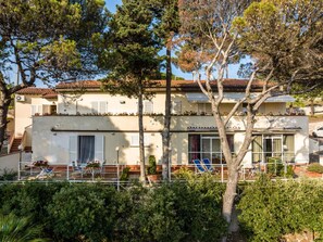 A two-story building with a tiled roof, a balcony with outdoor furniture, and a garden area.