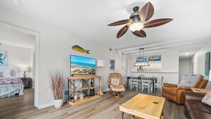 A spacious living room with a wooden floor, a ceiling fan, a television, and a dining area with a table and chairs. - La Mirage Condo 311 Beachfront Resort Condominiums with Private Boardwalk (Port Aransas)