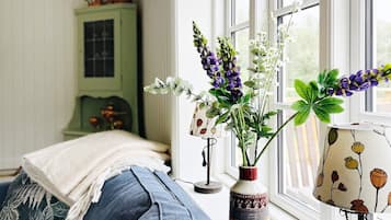 A bedroom with a bed, a window with a view, and a vase with flowers on the windowsill.