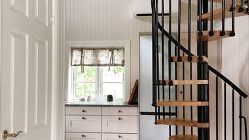 A kitchen with white cabinetry, a window with floral curtains, and a black spiral staircase.