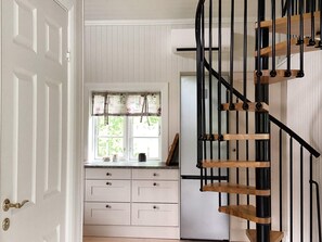 A kitchen with white cabinetry, a window with floral curtains, and a black spiral staircase.