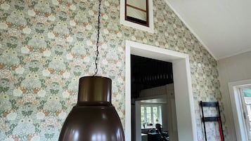 A room with a hanging pendant light, floral wallpaper, a window with a view, and a door leading to another room.
