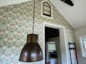 A room with a hanging pendant light, floral wallpaper, a window with a view, and a door leading to another room. - 4 Person Holiday Home in Allingsas, Sverige (Alingsas)