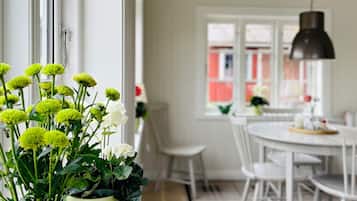 A dining area with a white table and chairs, a potted plant with flowers, and a window with a view of buildings.