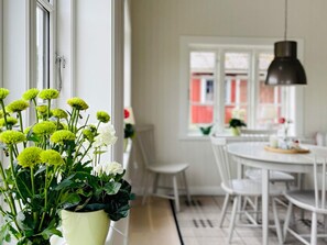 A dining area with a white table and chairs, a potted plant with flowers, and a window with a view of buildings. - 4 Person Holiday Home in Allingsas, Sverige (Alingsas)