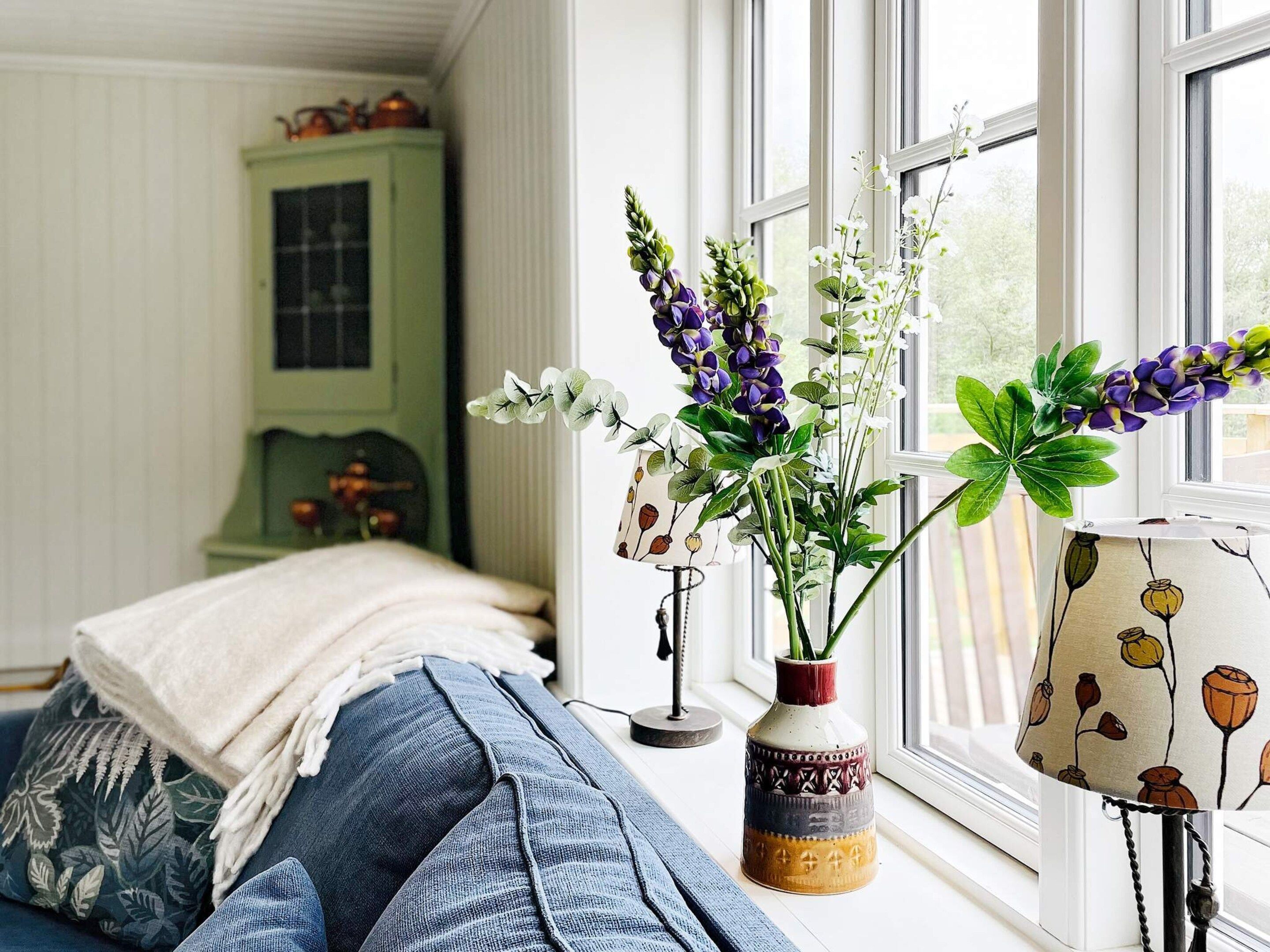Une chambre à coucher avec un lit, une fenêtre donnant sur un beau paysage et un vase rempli de fleurs posé sur le rebord de la fenêtre.