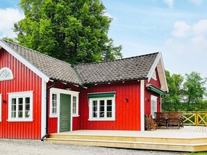 A red building with a green door and windows, a wooden deck with chairs, and a tree in the background. - 4 Person Holiday Home in Allingsas, Sverige (Alingsas)