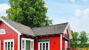 A red building with a green door and windows, a wooden deck with chairs, and a large tree in the background. - 4 Person Holiday Home in Allingsas, Sverige (Alingsas)