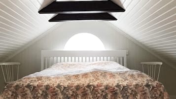 A bedroom with a sloped ceiling, a bed with a floral bedspread, and a skylight.