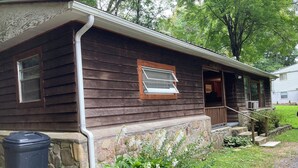 Una casa de madera con cimientos de piedra, un porche delantero y una ventana con marco de madera.
