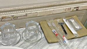 A bathroom with a marble countertop, two clear glass tumblers, a toothbrush, toothpaste, and a razor. - Blue Diamond Hotel (Hong Gai)