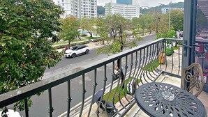 A balcony with a metal railing, a round table, and a chair. In the background, there are tall buildings and a street with cars. - Blue Diamond Hotel (Hong Gai)