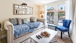 Ein Wohnzimmer mit Sofa, Couchtisch und Sessel. Ein Balkon mit Geländer und Blick ins Freie ist vorhanden.