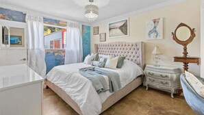 Une chambre à coucher avec un grand lit, une commode, un miroir et des œuvres d’art accrochées aux murs.