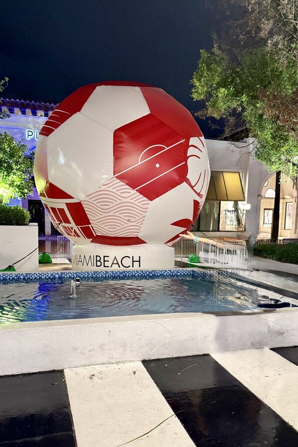 Un grand ballon gonflable sur lequel est inscrit le mot « MIAMIBEACH », placĂ© au bord dâune piscine.