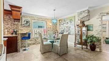 A dining area with a stone wall, a glass table, and two upholstered chairs.