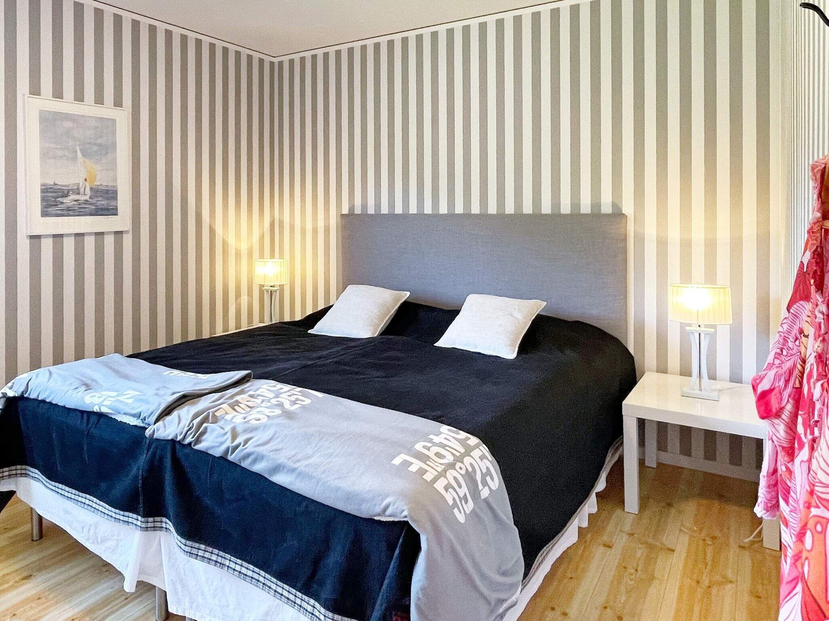 A hotel room with a bed, two bedside lamps, a striped wall, and a framed picture on the wall.