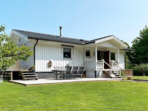 Une maison blanche avec un porche, une cheminée et une petite terrasse avec des chaises.