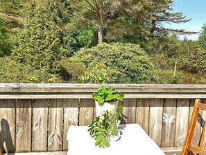 A white table with a potted plant in the center, set against a wooden fence with a backdrop of dense green foliage. - 6 Person Holiday Home in Uddevalla (Uddevalla)