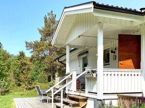 Une maison en bois blanche, avec un porche, une porte en bois et une fenêtre ornée d’une horloge.