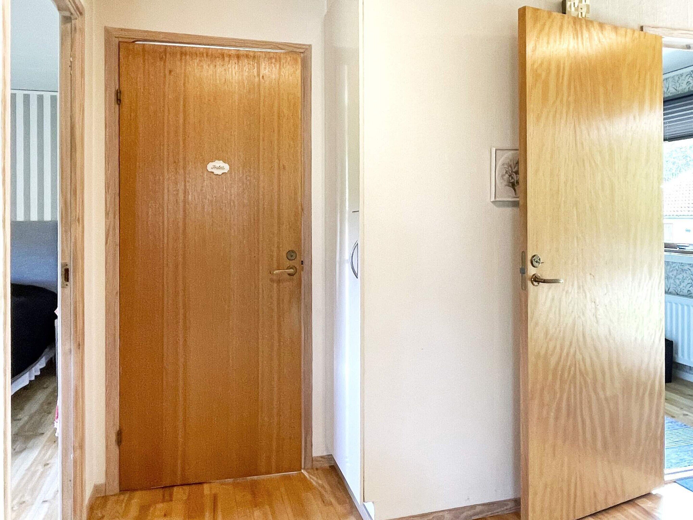 A wooden door with a handle and a lock, adjacent to a wall with a light switch and a small electrical outlet.