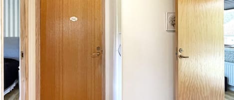 A wooden door with a handle and a lock, adjacent to a wall with a light switch and a small electrical outlet.
