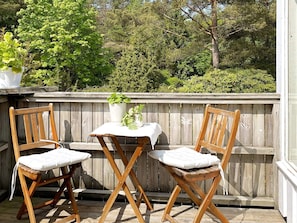 Une terrasse en bois avec deux chaises en bois et une petite table, entourée d’une clôture en bois et de verdure.