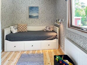 A child's bedroom with a bed, pillows, stuffed animals, a window, and a radiator.