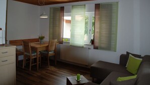 A cozy living room with a wooden ceiling, a dining area with a table and chairs, and a sofa with cushions.
