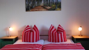 A bedroom with a bed, two bedside lamps, and a painting of a forest on the wall.