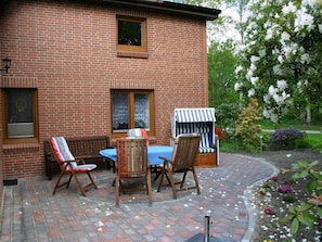 A brick building with a patio area featuring a table and chairs, a striped umbrella, and a garden with flowers. - Elke Luthje Modern Retreat (Hochdonn)