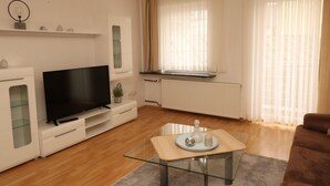 A modern living room with a flat-screen TV, a glass coffee table, and a brown sofa.