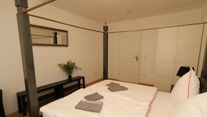 A bedroom with a four-poster bed, a bedside table with a plant, and a wardrobe with a mirror.