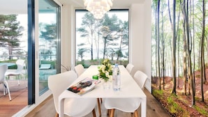 A modern dining area with a white table, chairs, and a hanging light fixture. - Villa Vogue, Austernfischer (Binz)