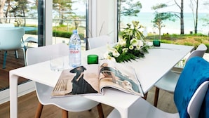 A modern dining area with a table, chairs, a magazine, a water bottle, and a floral arrangement. - Villa Vogue, Austernfischer (Binz)