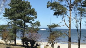 A coastal area with a sandy beach, trees, and a person walking. - Villa Vogue, Austernfischer (Binz)