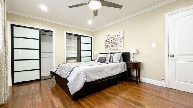 A bedroom with a bed, a ceiling fan, a nightstand, a painting, and a door. - Gourmet Kitchen + Private Front Yard + Parking (San Jose)